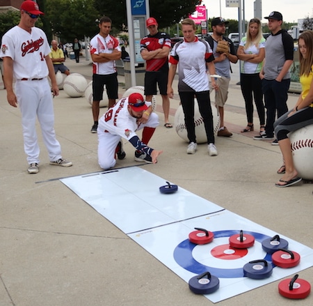Winnipeg Goldeyes pitcher Duke Von Schamann attempts an in-turn takeout in his introduction to curling, encouraged by teammate Jacob Rogers and several of Manitoba’s elite young curlers. (Photo, courtesy Winnipeg Goldeyes). 
